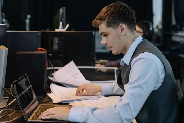 Young male professional focused on work with laptop and documents at office desk. Rechtsformwahl in der Schweiz: Haftung, Steuern und Kapital